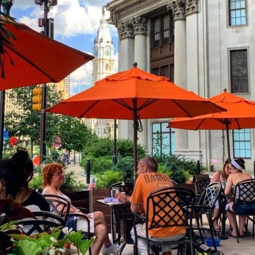 Guests on the patio under orange umbrellas on the Benjamin Franklin Parkway